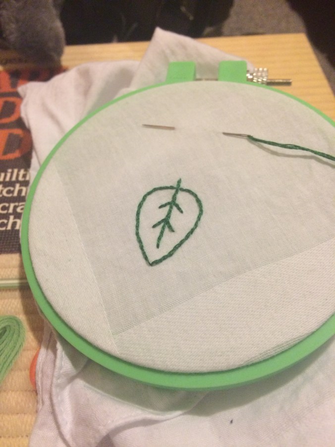 a little green leaf embroidered onto a white handkerchief corner