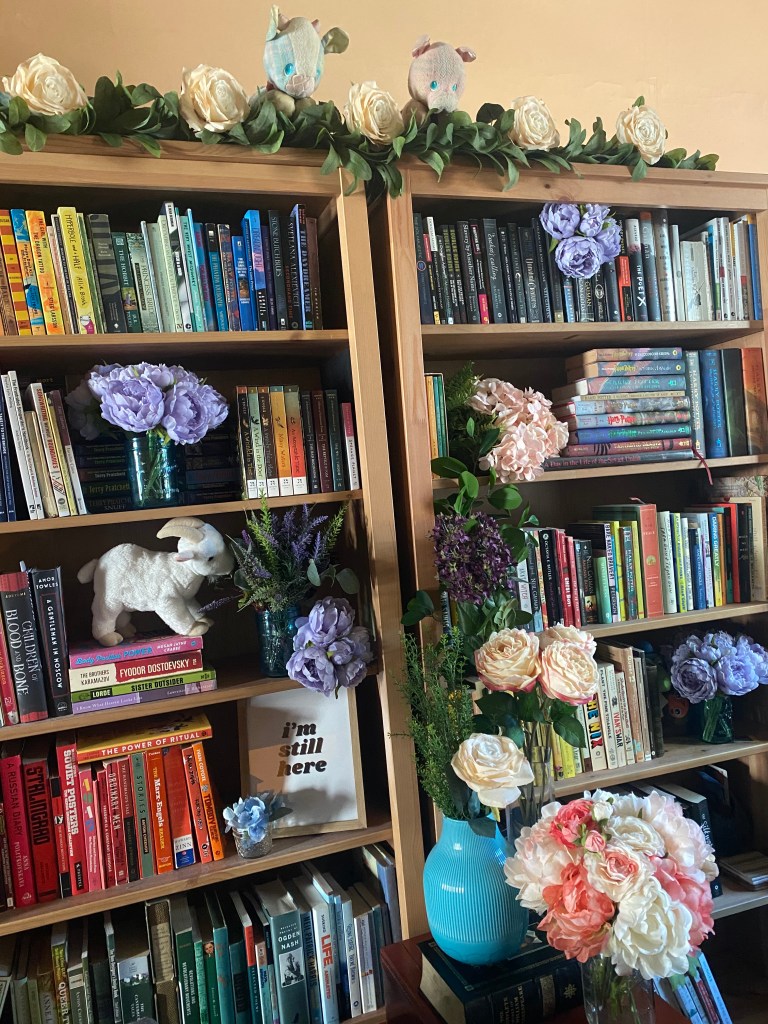 Wedding backdrop - bookshelves organized by color, with all sorts of silk flowers arranged artfully among the books.